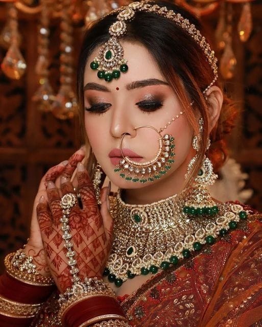 Traditional red HD bridal makeup in Lucknow by AAINA Salon — emerald polki jewellery look
